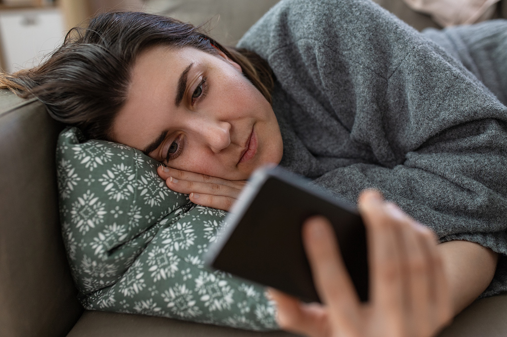 une femme est allongée sur le canapé en train de faire défiler son téléphone.