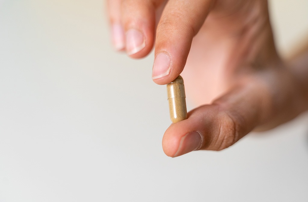 Quelqu’un montre une capsule entre deux doigts.